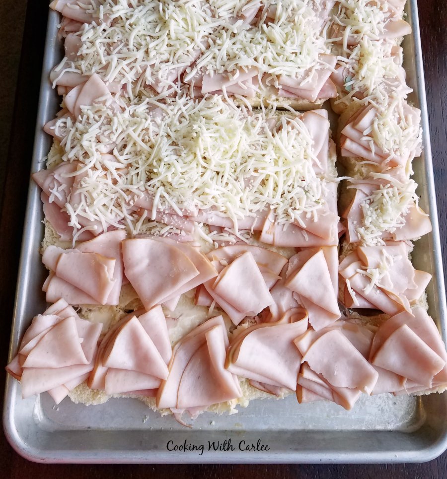 tray of partially assembled sliders with cheese, ham and turkey.