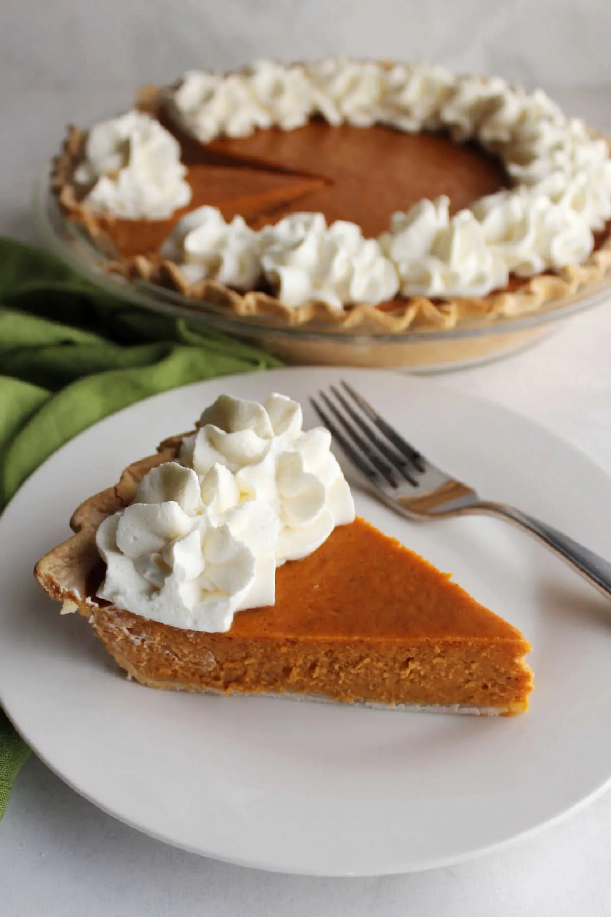 Sliced of pumpkin pie on plate topped with whipped cream and a fork nearby, ready to eat.