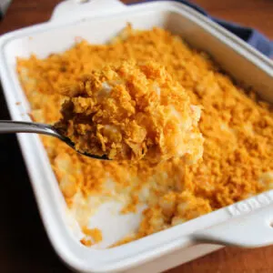 Serving spoon getting a big scoop of french onion cheesy potato casserole topped with golden brown cornflake crumbs.