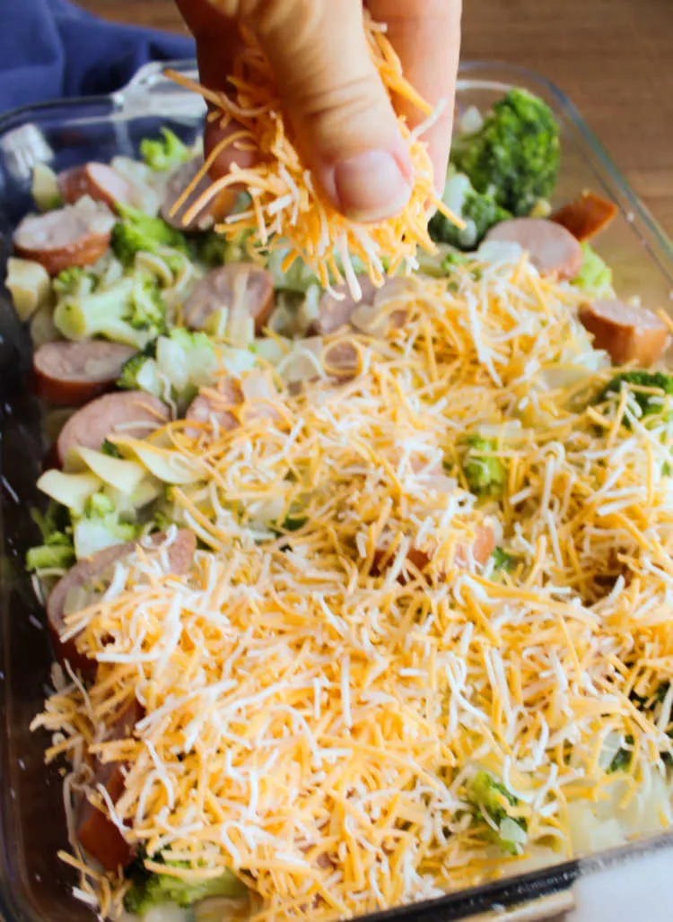 sprinkling cheese over broccoli, pasta and sausage.