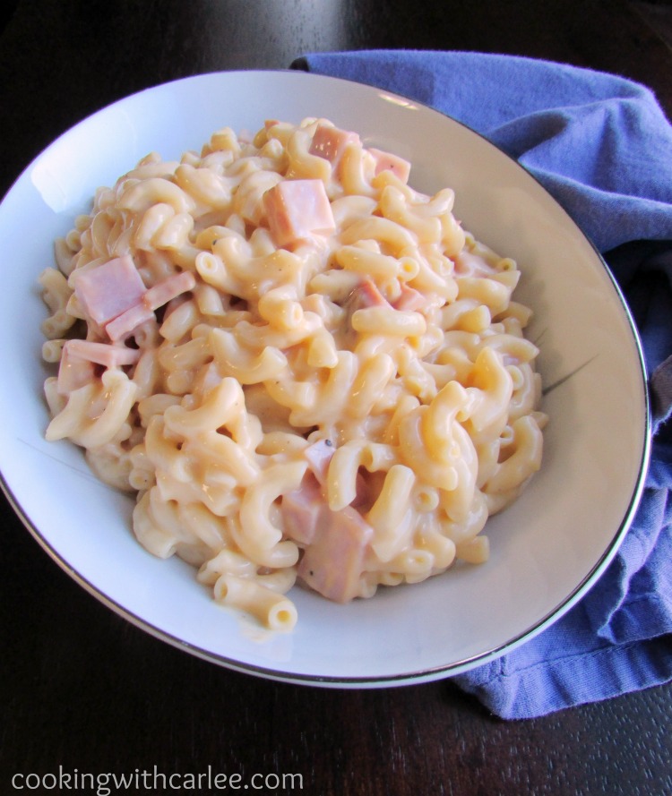 Serving bowl filled with creamy macaroni and cheese with chunks of ham in it.