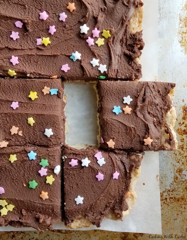 Big sheet of sugar cookie bars with chocolate frosting and sprinkles, some bars cut and one slightly pulled away from the rest