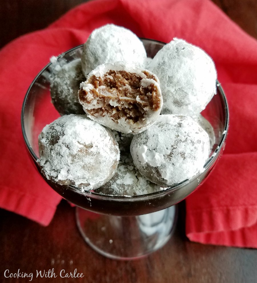 bowl of rum balls coated in powdered sugar, one with bite missing revealing brown center