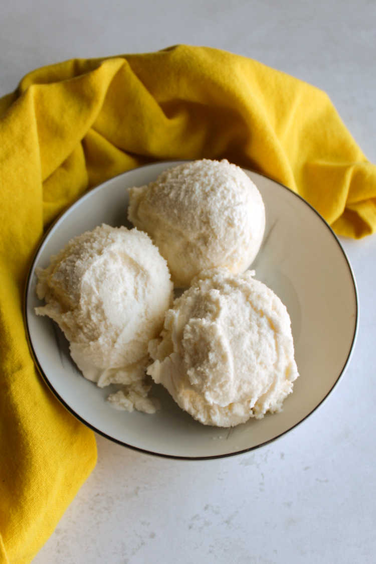 small bowl with three scoops of creamy homemade lemon ice cream and yellow napkin.