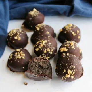 Peanut butter oreo balls dipped in chocolate and topped with chopped peanuts, one cut in half showing rich chocolaty center.