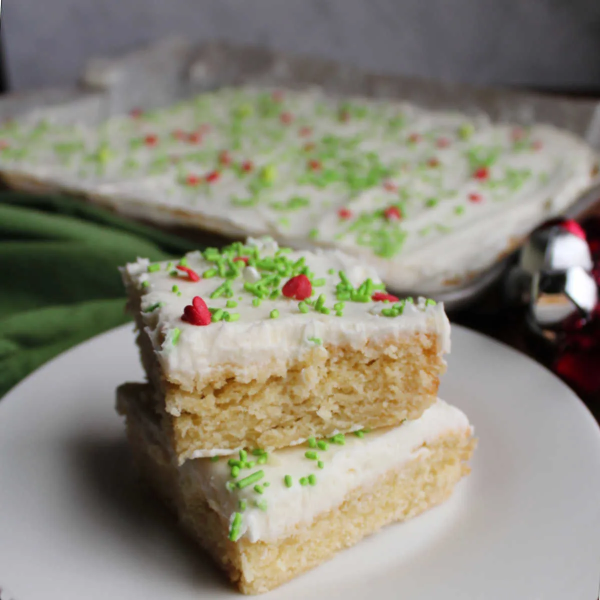 Plate with two frosted sugar cookie bars topped with white frosting and sprinkles stacked on top of each other.