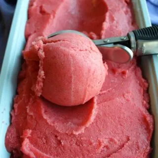 Ice cream scoop getting a ball of pink strawberry orange sorbet.
