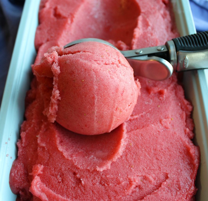 Ice cream scoop getting a ball of pink strawberry orange sorbet.
