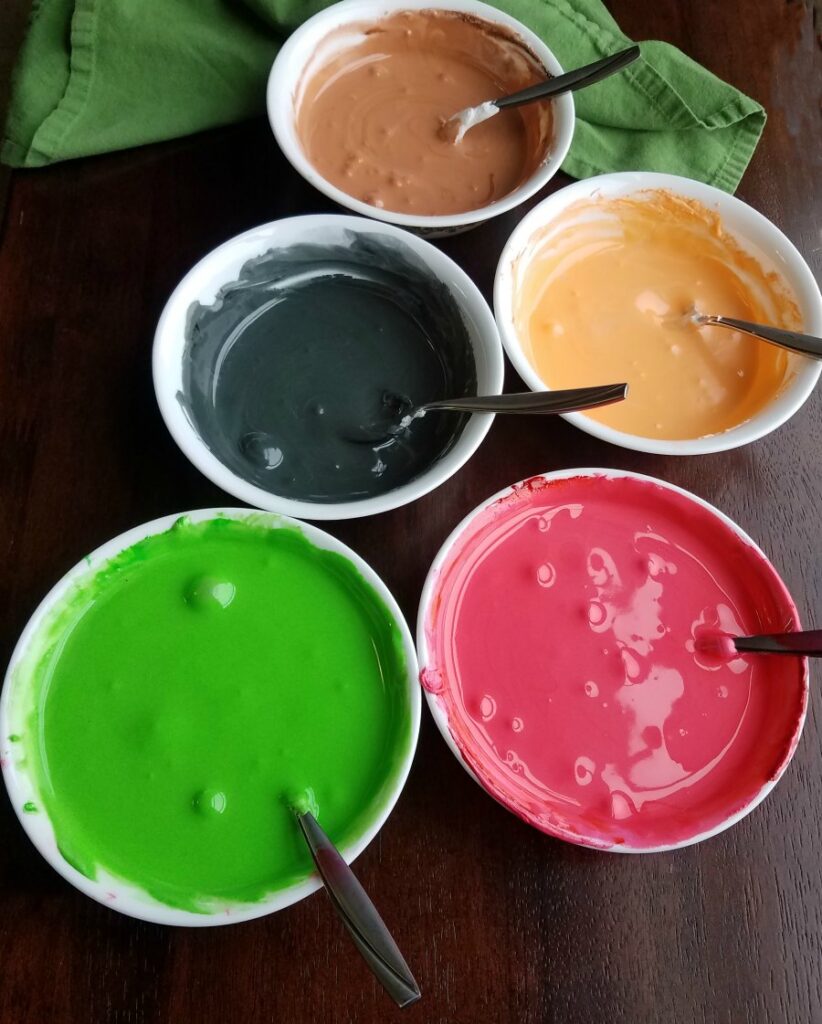 bowls of colored thinned out royal icing ready for cookies. 