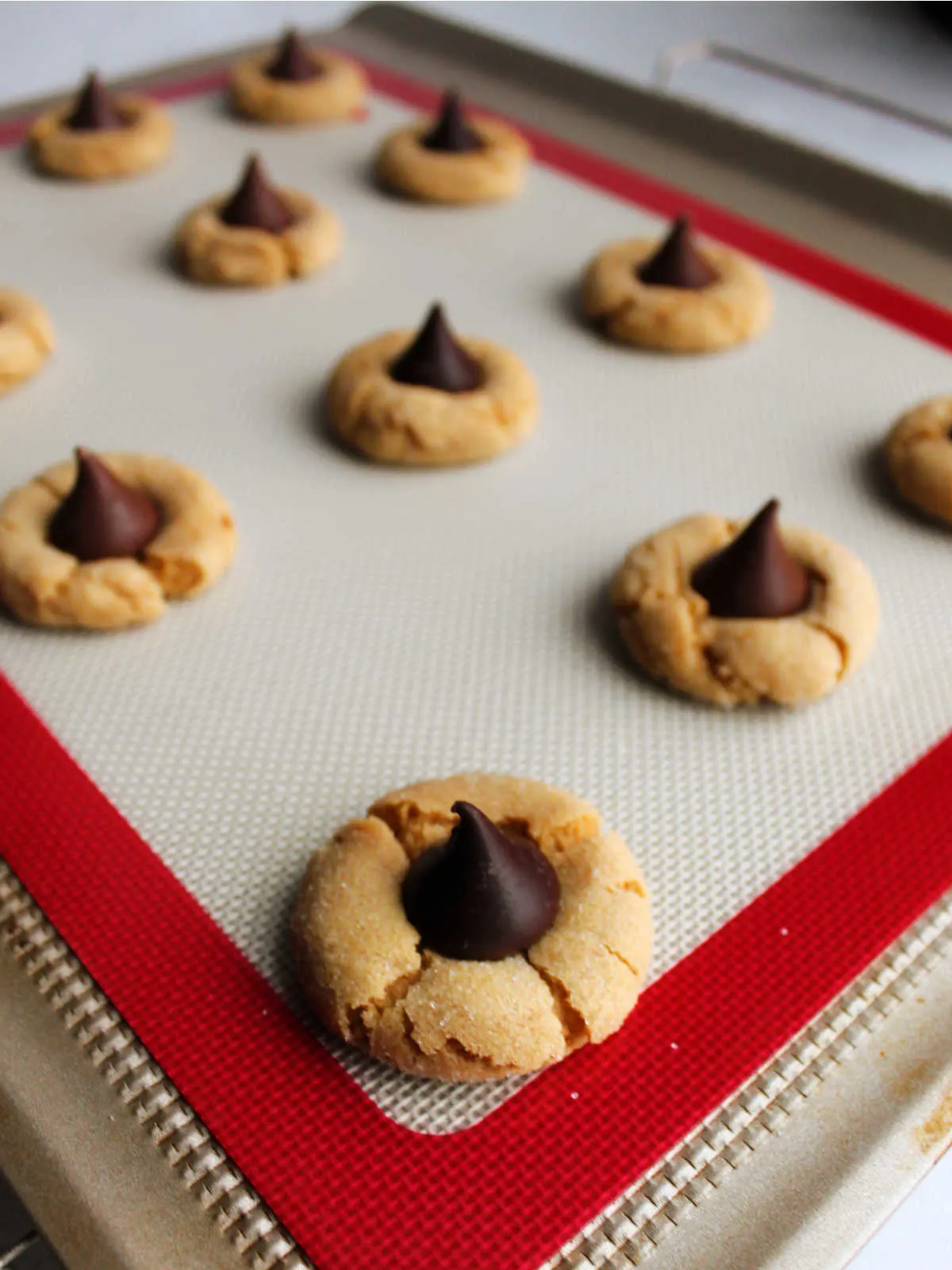 Cookie sheet with unwrapped Hershey's Kisses pressed into the center of soft peanut butter cookies. 