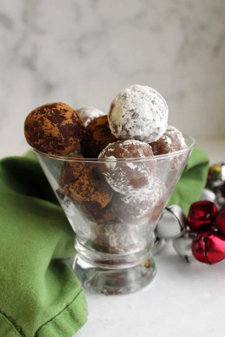 glass filled with rum balls, some coated in cocoa powder and some in powdered sugar.