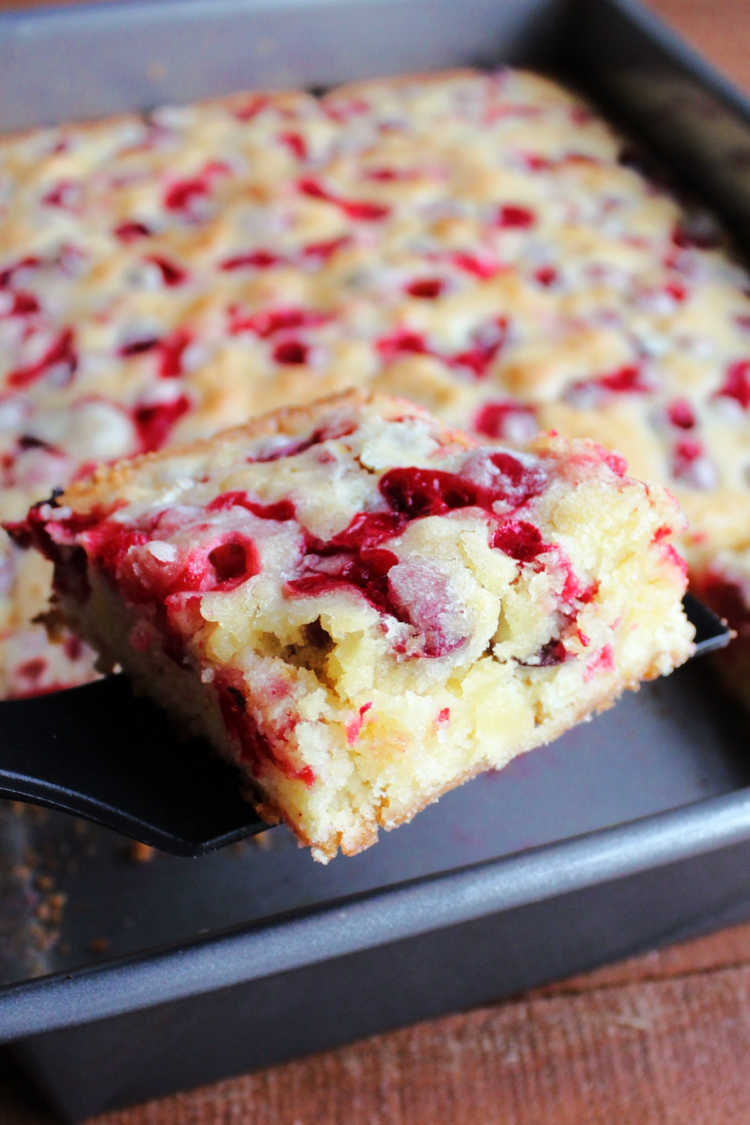 lifting piece of cranberry snack cake out of pan with bright berries showing.
