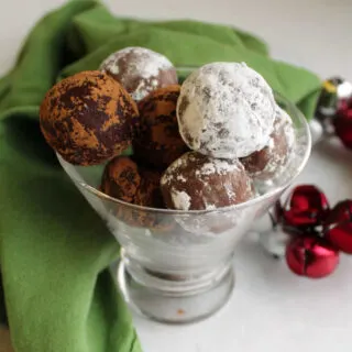 Stemless martini glass filled with powdered sugar and cocoa powder dusted rum balls ready to eat.