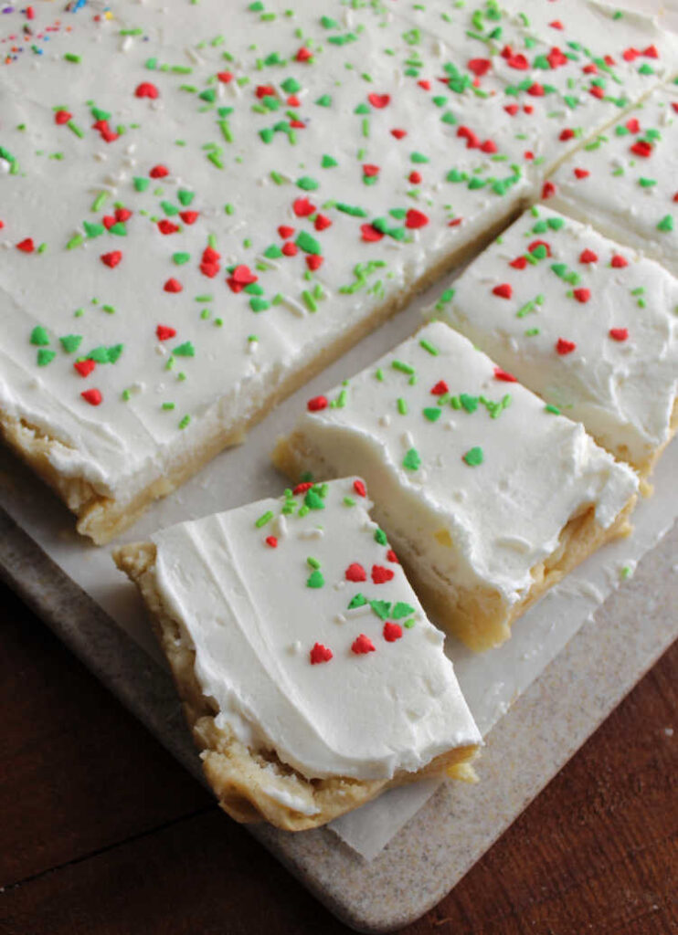 pieces of sugar cookie bar topped with white buttercream being cut off from big cookie.