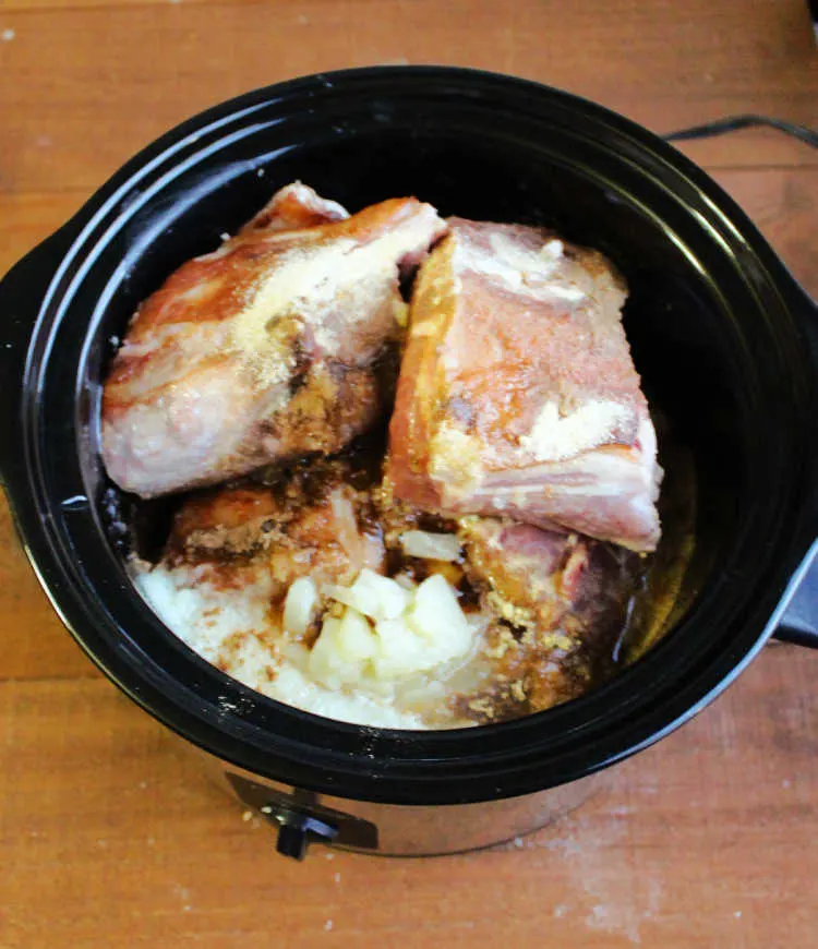 slow cooker filled with hunks of browned pork shoulder, pineapple and spices.