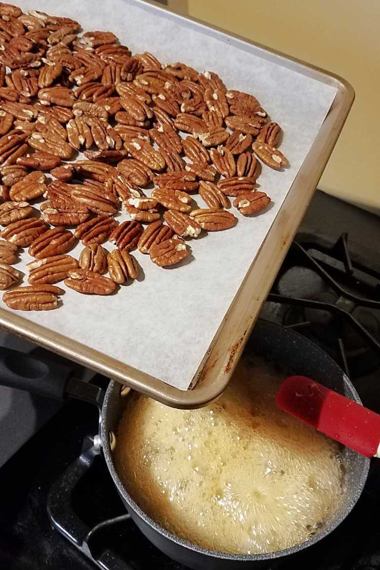 baking sheet of toasted pecans being dumped into saucepan of boiling honey.