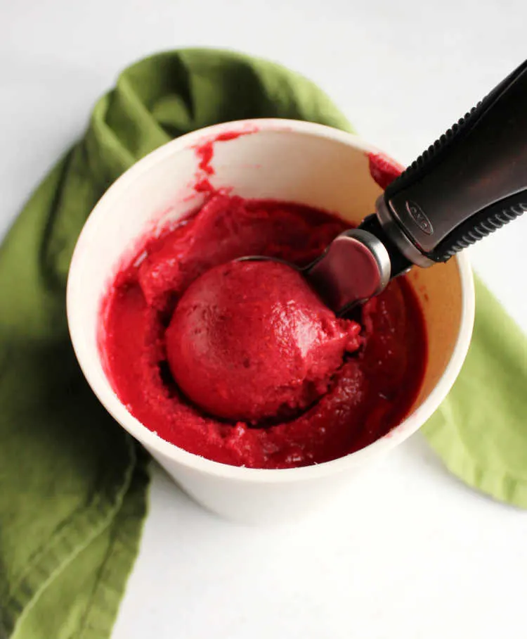 Scooping ball of raspberry sorbet in storage container.