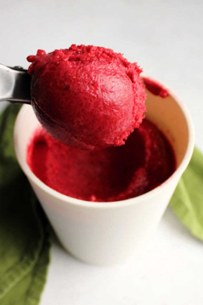 scoop of raspberry sorbet being lifted out of container.