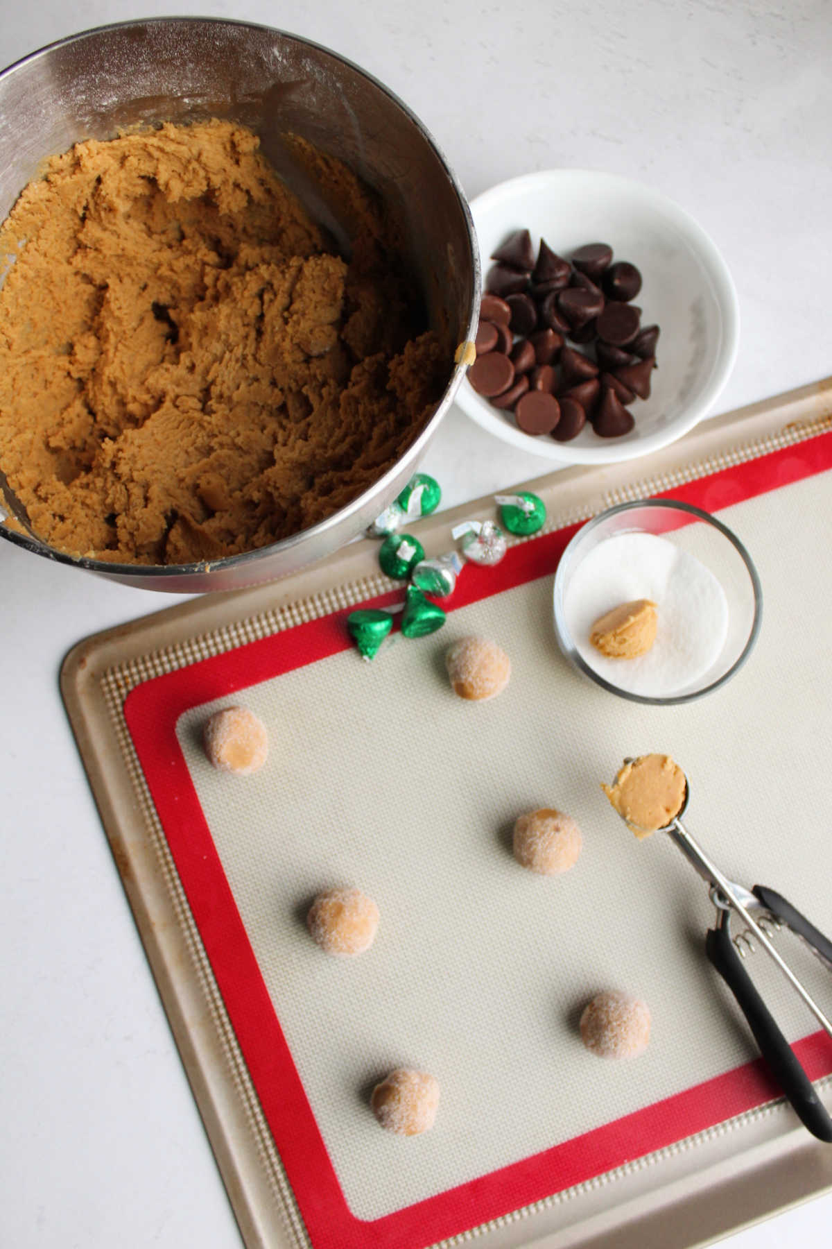 Mixer bowl of peanut butter cookie dough being rolled into balls to become blossom cookies.