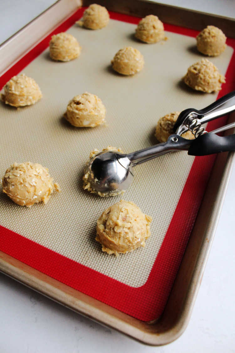 small cookie scoop with balls of dough on silicone mat lined cookie sheet pan.
