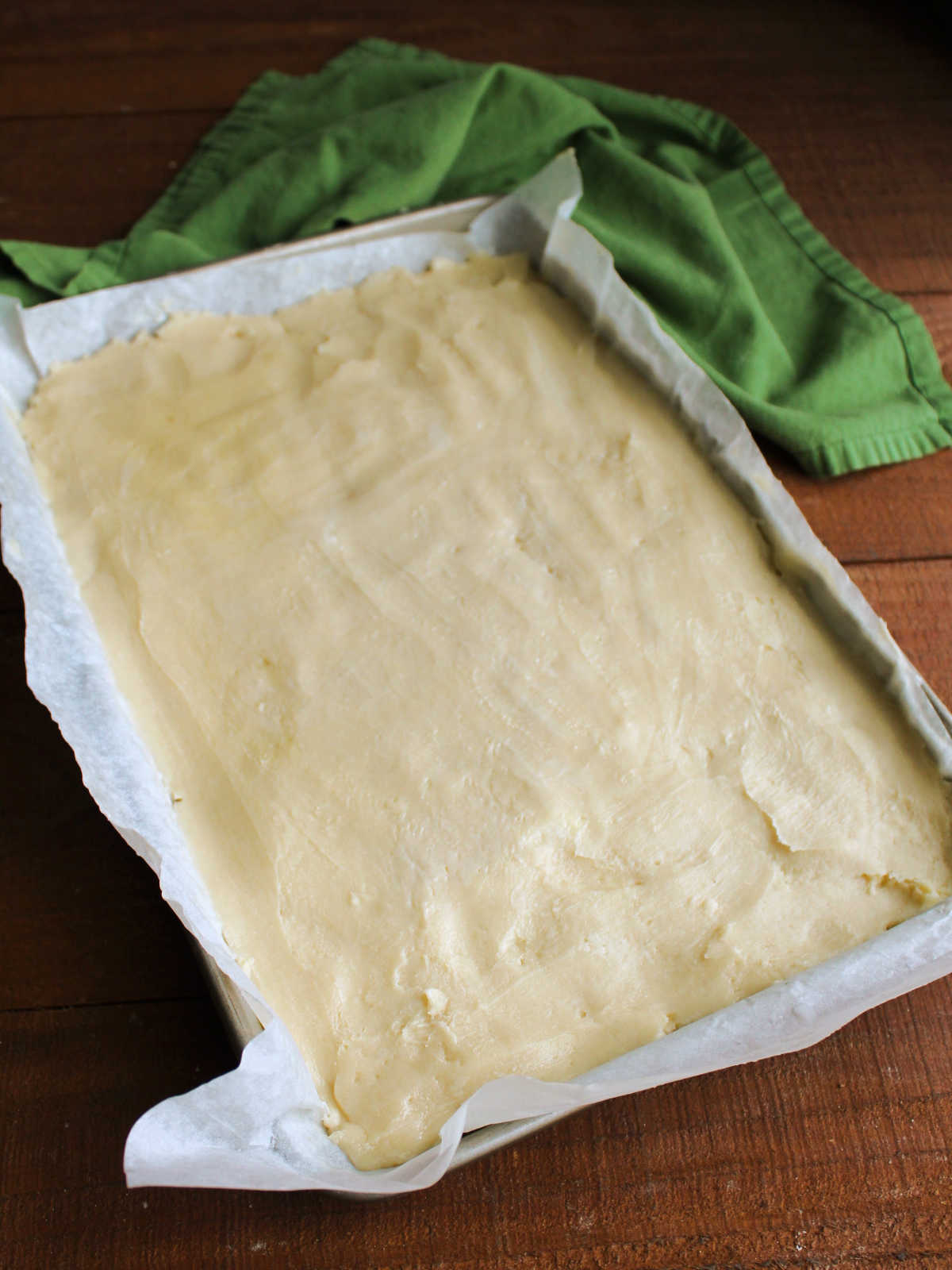Sugar cookie dough pressed into parchment paper lined bar pan.