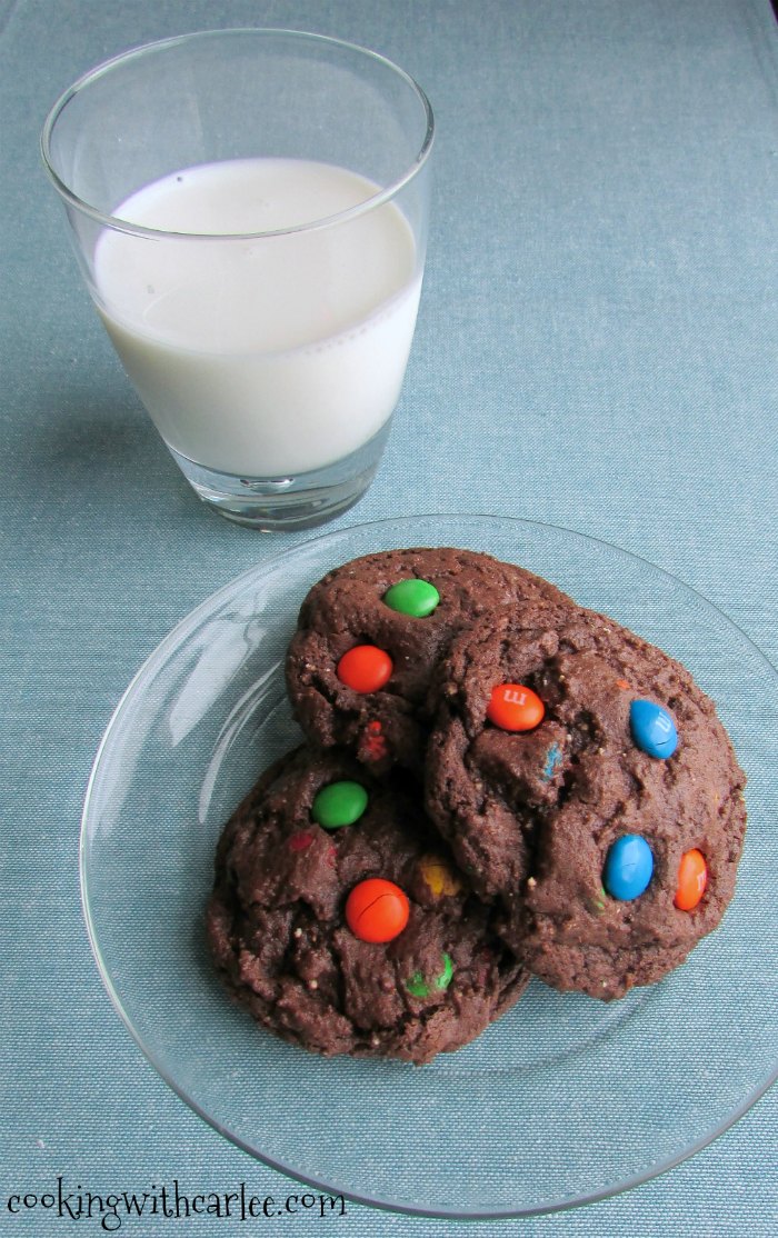 Pile of double chocolate m&m cookies with a cup of milk.