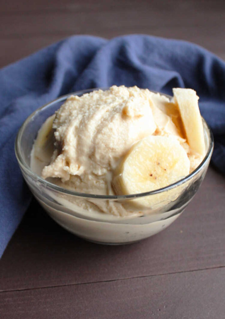 peanut butter and banana ice cream in glass bowl with slices of bananas on top.