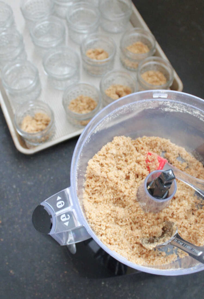 graham cracker crumbs in food processor and some spooned into jars for cheesecake crust