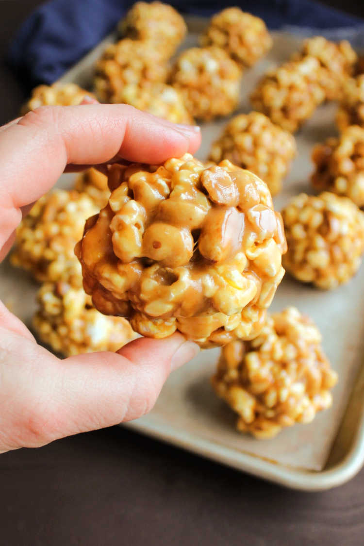 Hand holding peanut butter popcorn ball with roasted peanuts inside.