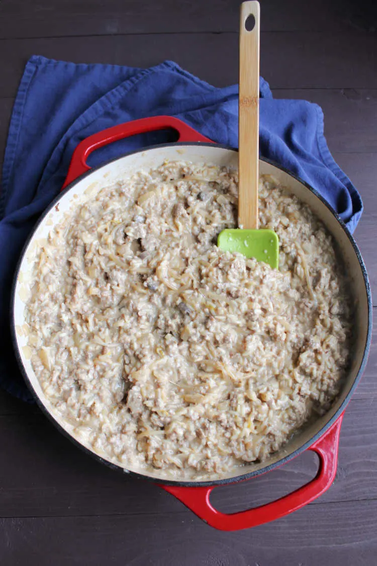 enameled cast iron skillet filled with creamy rice loaded with bean sprouts and ground pork.