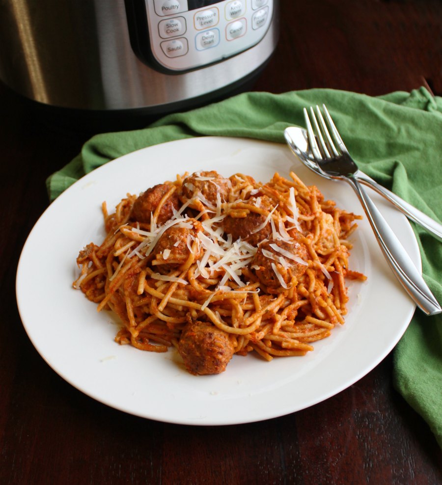 plate of spaghetti and meatballs in front of pressure cooker.