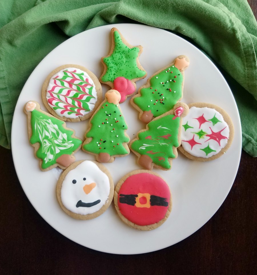 plate of christmas shaped peanut butter cut out cookies decorated with royal icing.