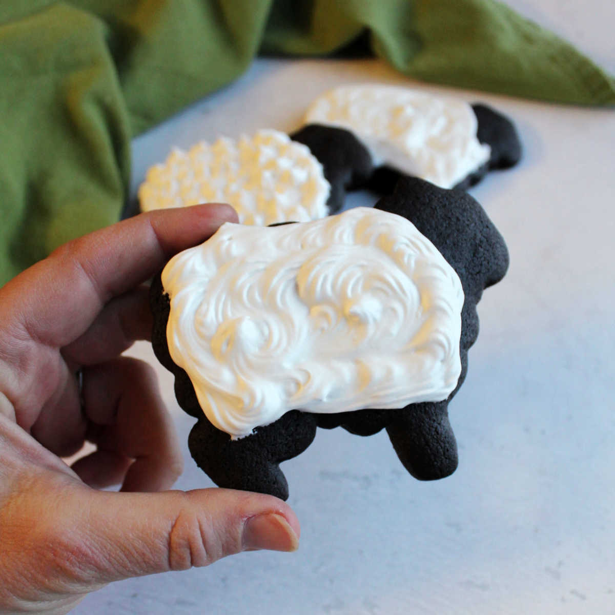 dark chocolate cookies in the shape of sheet with white royal icing fleece on top.