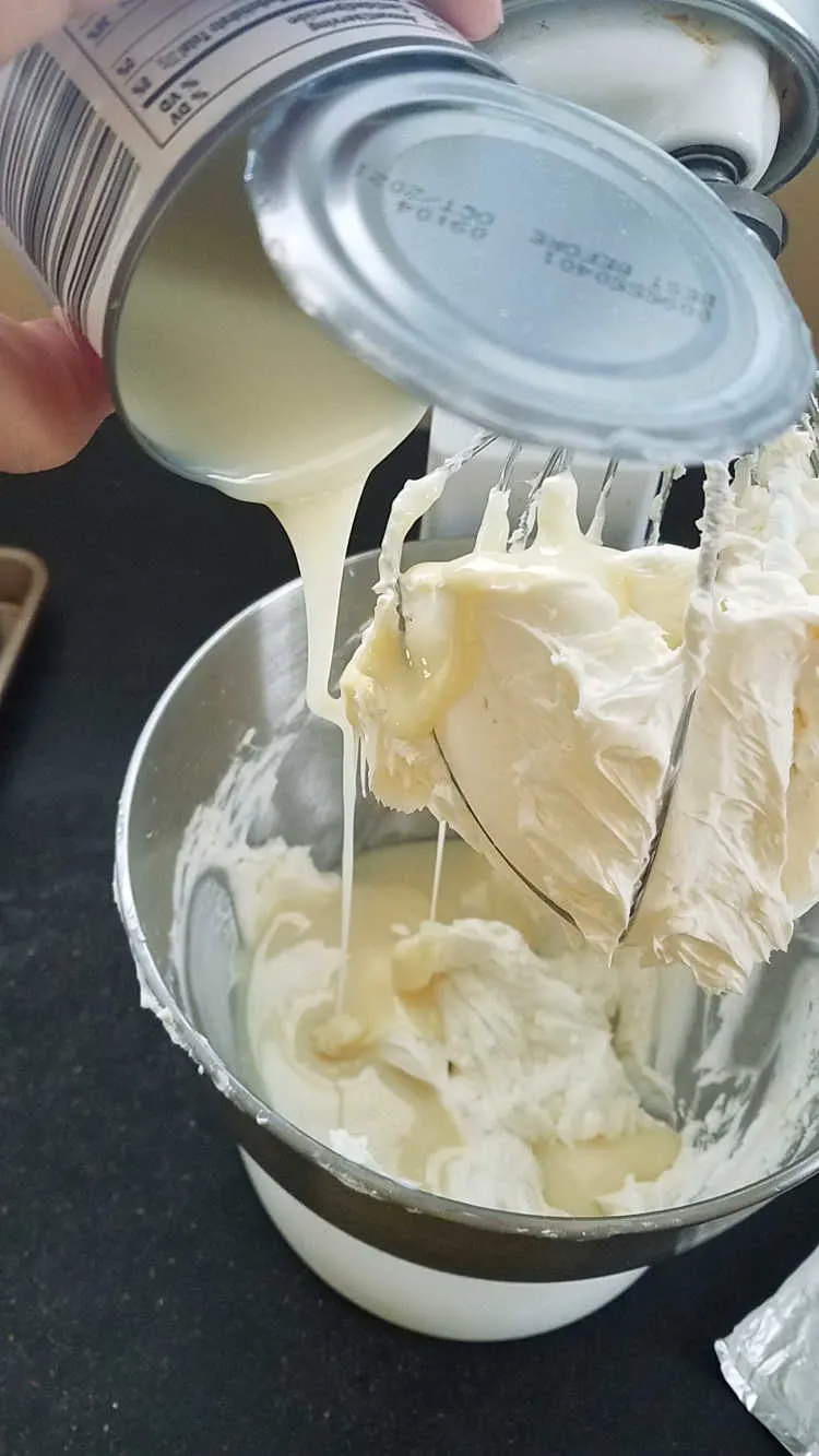 pouring sweetened condensed milk into mixer full of whipped cream cheese