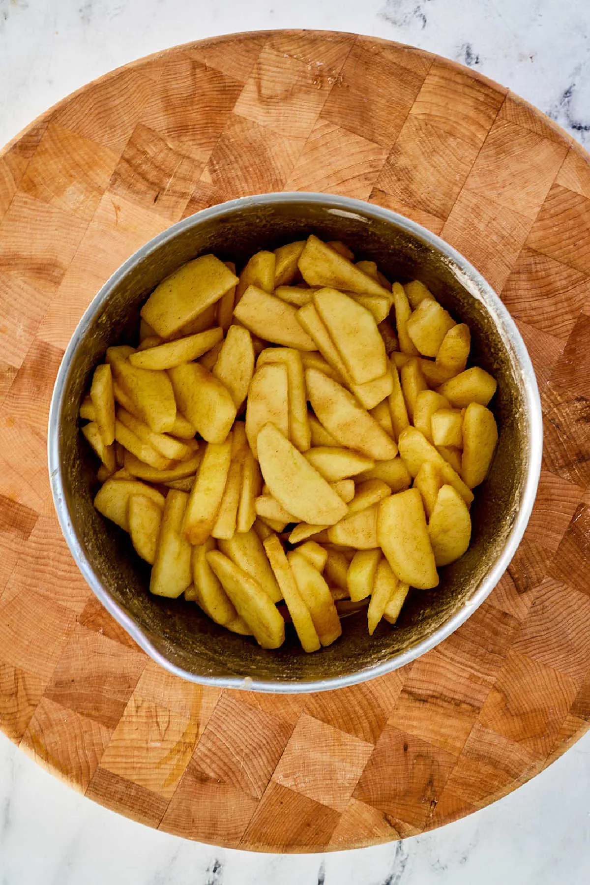 Mixing bowl of peeled apple slices tossed in cinnamon sugar mixture.
