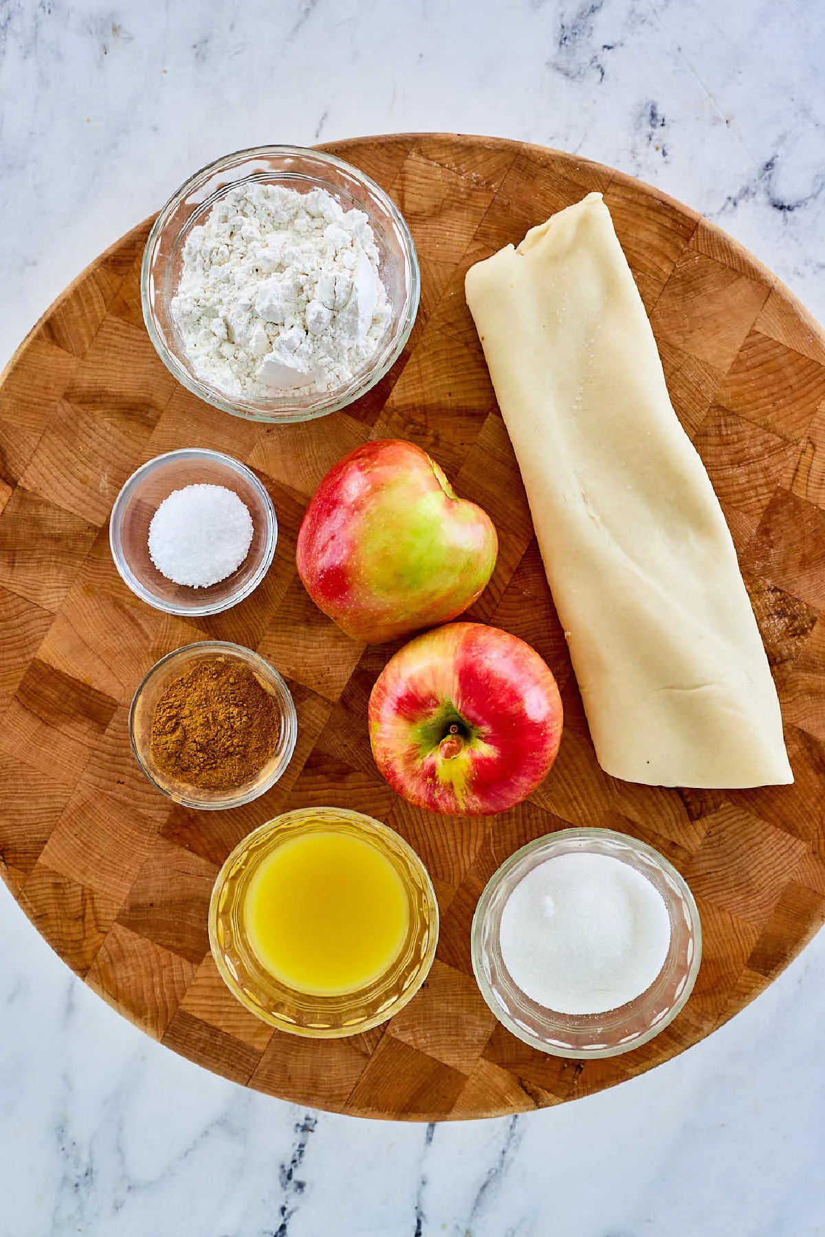 Ingredients including apples, orange juice, sugar, cinnamon, flour, and pastry ready to be made into a deep dish apple pie. 