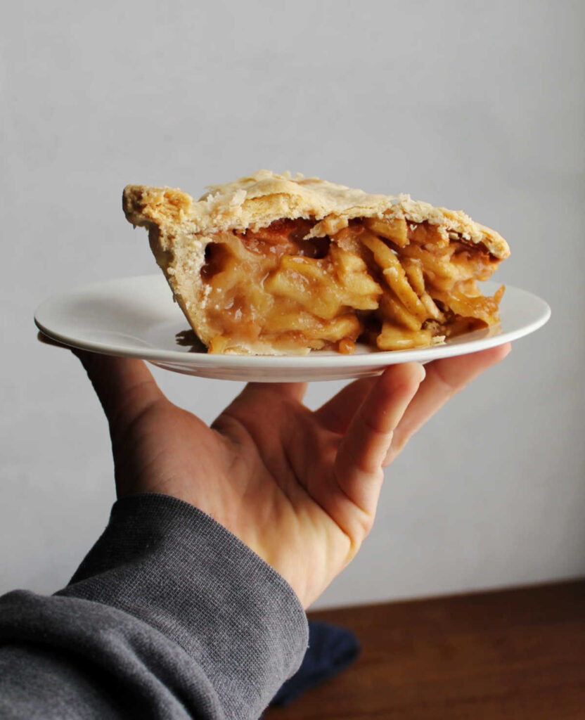 hand holding plate with slice of apple pie on it.