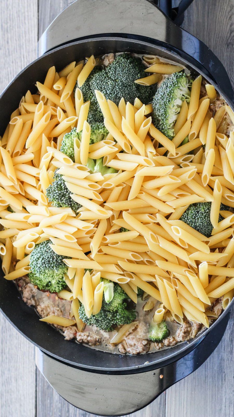adding pasta and broccoli to pot with browned Italian sausage