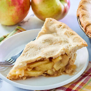 Piece of old fashioned apple pie with lots of tender cinnamon spiced apple slices and tender pie crust on top.