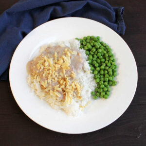 dinner plate filled with peas and rice topped with creamy tuna mixture and crunchy potato chips.
