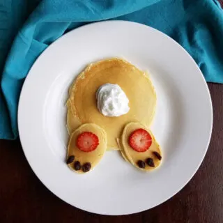 Pancakes decorated to look like bunny butt with whipped cream tail and strawberry and raisin feet.