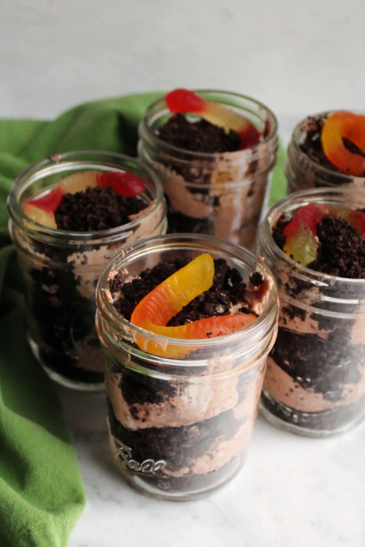 Jars of dirt pudding with layers of Oreo crumbs, chocolate pudding mixture and a gummy worm on top.