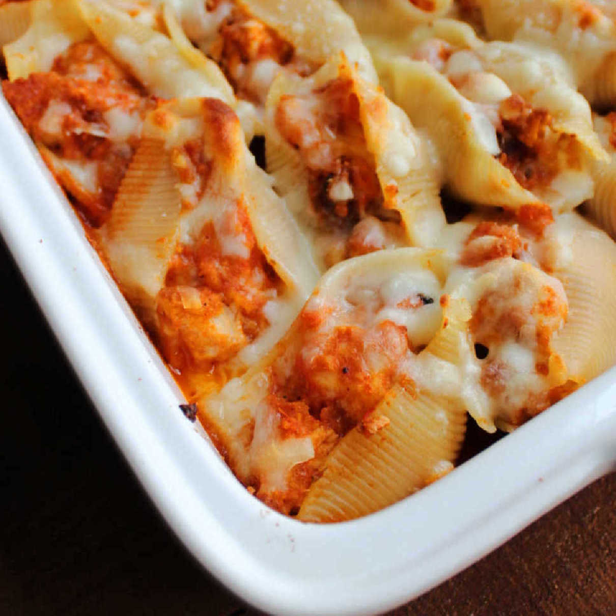 Close up on the corner of a pan of stuffed shells filled with chicken, tomato sauce and cheese.