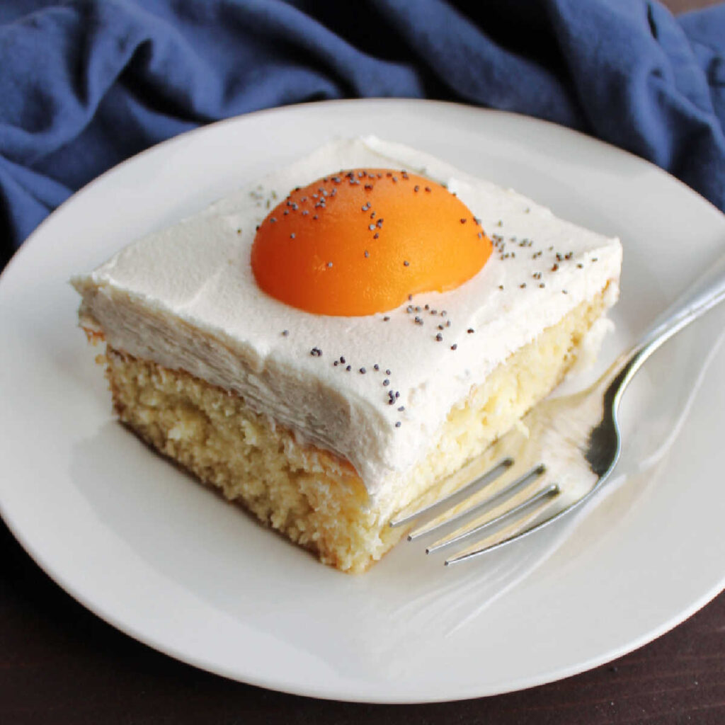 close square of vanilla sheet cake topped with white icing and apricot half to look like a fried egg.