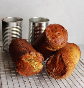 can shaped date nut bread cooling on wire rack with cans in background.