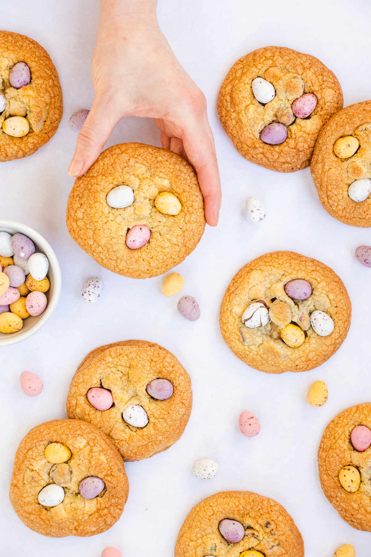 Hand holding large golden brown cookie with mini chocolate eggs on top.