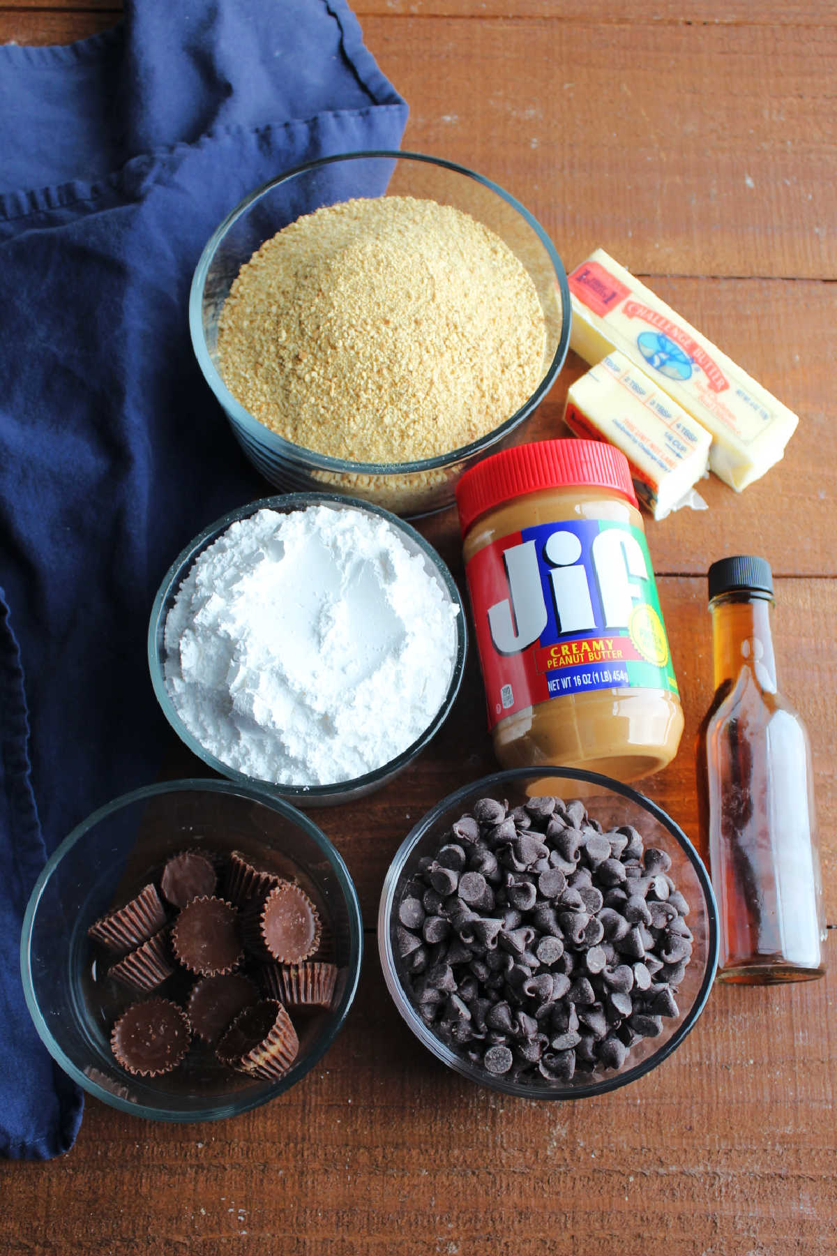 Ingredients: creamy peanut butter, powdered sugar, graham cracker crumbs, butter, vanilla, chocolate chips and peanut butter cups ready to be made into peanut butter bars.