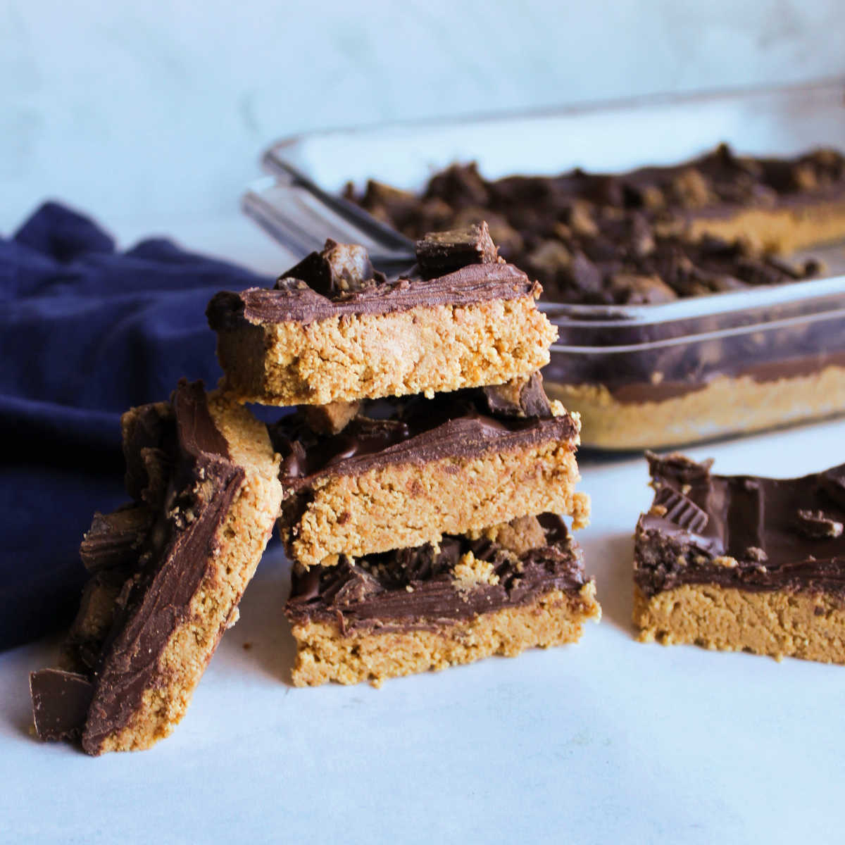 Stack of peanut butter bars topped with chocolate topping and chopped peanut butter cups.