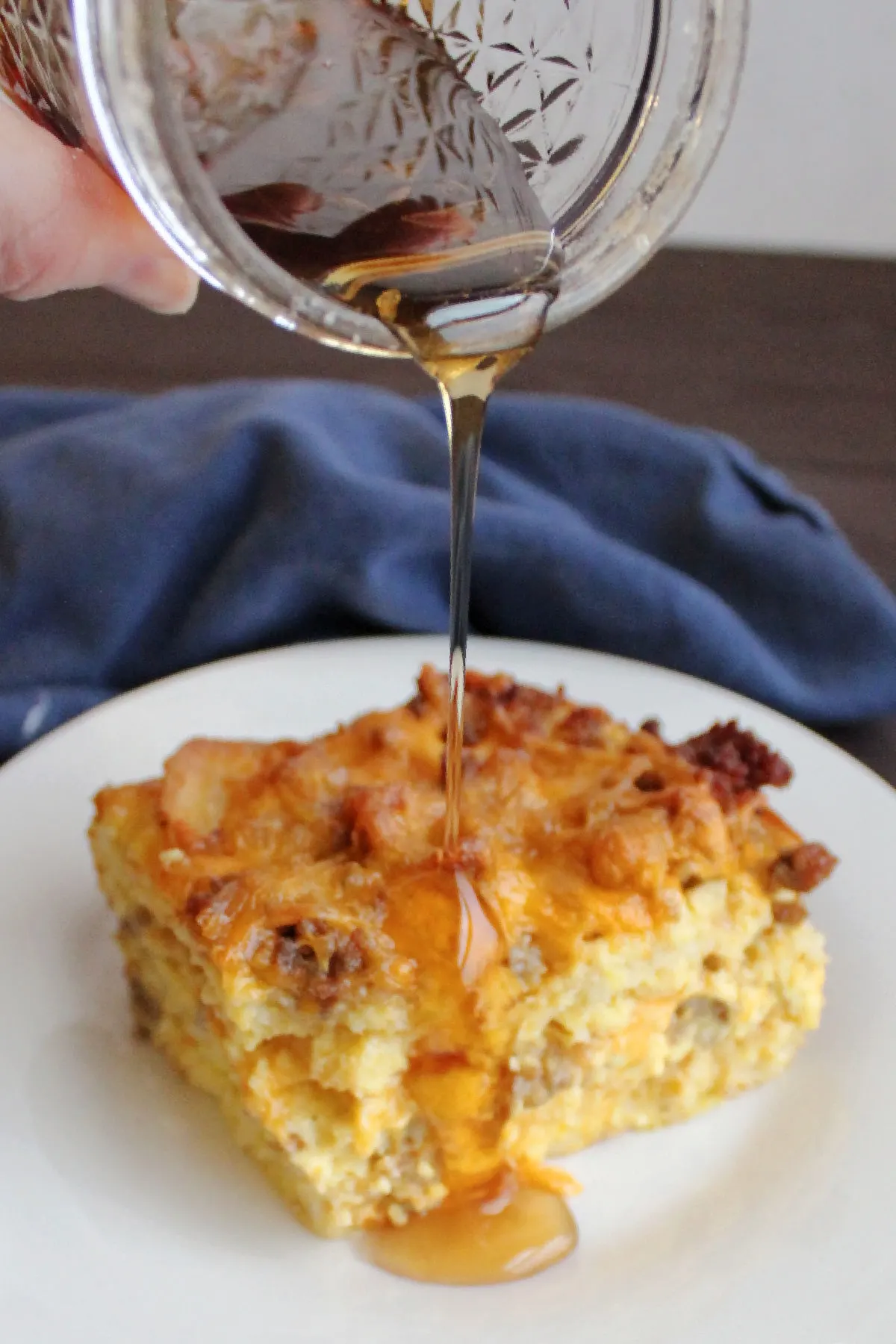 pouring maple syrup over a piece of waffle, egg and sausage casserole.