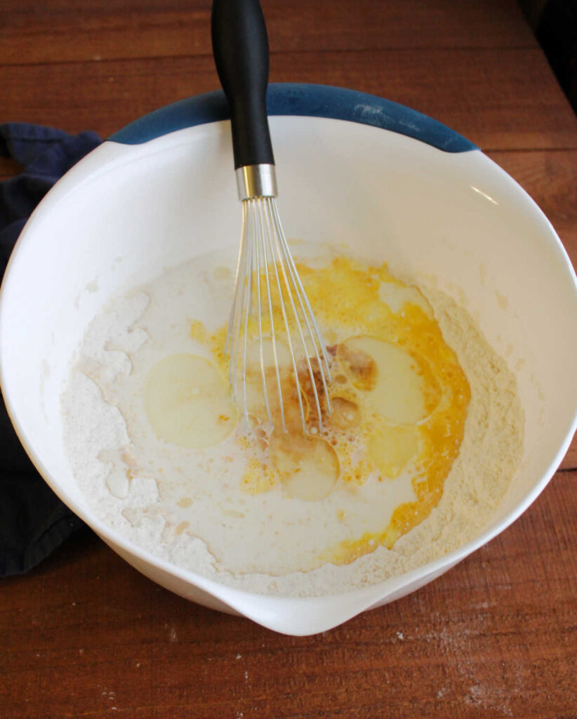 large mixing bowl with pancake batter ingredients and whisk inside.